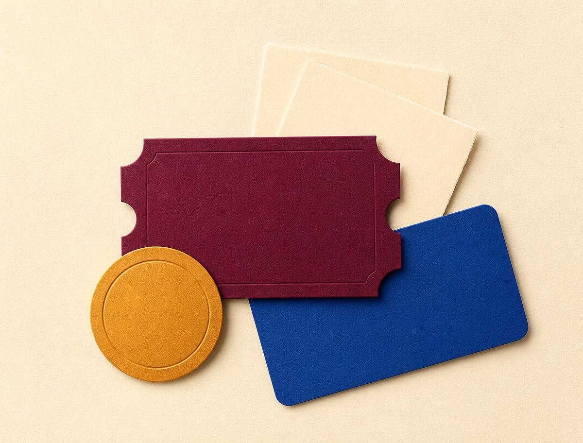 A burgundy ticket, blue card and gold coin arranged on cream paper
